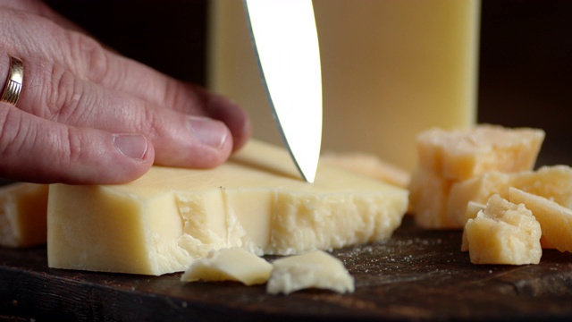 男人的手拿着一把刀，切下了几块帕尔玛干酪。