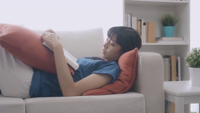 一个女人躺在沙发上看书。缓慢的运动。难过的时候,中景镜头。