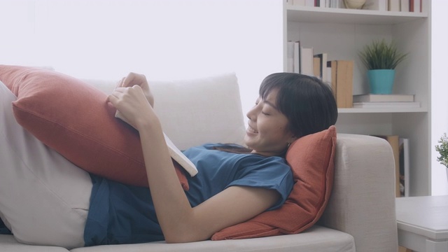 一个女人躺在沙发上看书。缓慢的运动。大笑,中景镜头。
