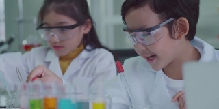 穿着科学家制服的亚洲孩子们玩得很开心。学习科学实验室实验试管玻璃水在桌子上各种颜色