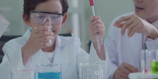 穿着科学家制服的亚洲孩子们玩得很开心。学习科学实验室实验试管玻璃水在桌子上各种颜色