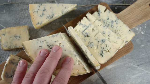 男性用手在砧板上切布里干酪。