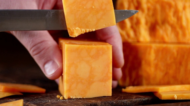 男用刀将切达干酪切成小块。