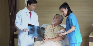一位年轻的亚洲医生用x光片向病人解释治疗后的症状。一位外科医生在医院病床上用平板电脑与一位老人交谈。