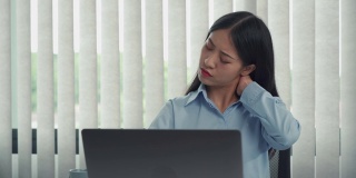 一位年轻的亚洲女性正坐在公司的办公室里，脖子很疼。