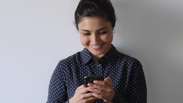 微笑的印度女性拿着智能手机与朋友在线聊天