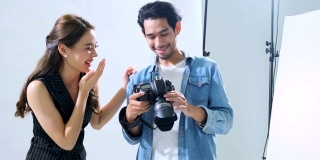 年轻的亚洲男性摄影师展示照片给女模特在相机显示手持拍摄