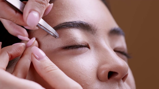 美容师在化妆前拔除年轻的亚洲女人的眉毛