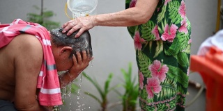 亚洲华人老年妇女洗她的丈夫的头发，洗头在前院当没有水供应