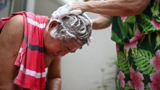亚洲华人老年妇女洗她的丈夫的头发，洗头在前院当没有水供应视频素材模板下载