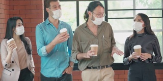 一群办公室工作人员戴着口罩在办公室走动和交谈，以保护COVID-19