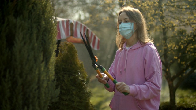年轻的女孩在花园里工作，戴着防护面具，修剪灌木