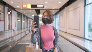 亚洲妇女戴着口罩，在机场通过智能手机进行视频会议视频素材模板下载