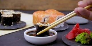 拿一个用竹筷夹着的unagi寿司卷，放在黑色背景的酱油里，亚洲菜，日本菜