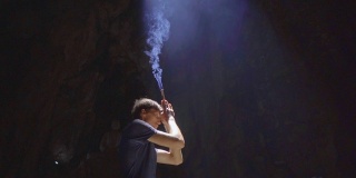 慢镜头拍摄的一个年轻的欧洲男子正在祈祷，手里拿着烟熏香棒。他是在大理石山中最大的石窟寺庙，一个佛教寺庙的综合体