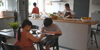 两个孩子在家学习写中国书法，而他们的母亲在厨房柜台准备食物
