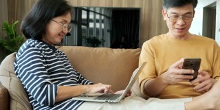 快乐的老人爷爷和奶奶放松，随意使用智能手机和笔记本电脑，花时间一起看有趣的有趣的积极的视频在线概念