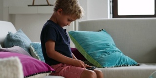 孩子坐在家里的沙发上使用智能手机。孩子拿着手机玩游戏