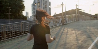 后视图。亚洲女性正在进行户外跑步锻炼。亚洲女运动员穿黑色运动服，而跑在桥上的人行道在城市。健康跑步和户外运动的概念