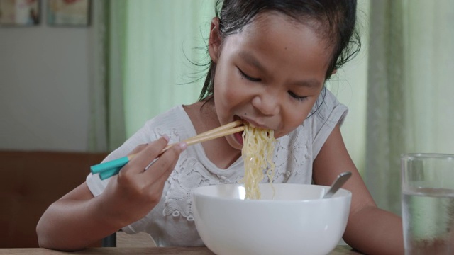可爱的亚洲小女孩在家里用筷子吃美味的方便面。慢动作镜头。