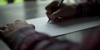 Kuchl /奥地利- 2019年8月22日:一名男子的手在白纸木桌上书写信件。复古信，婚礼爱情故事，新郎誓言。缓慢的运动。关闭了。阳台外的绿草。