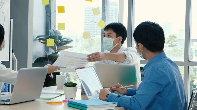 亚洲商人在医疗标志手握笔记纸会议与新的启动项目分享给业务团队。一群工人坐在桌边听演讲者讲话。商务会议的概念。
