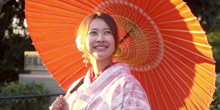 慢镜头近距离拍摄微笑的年轻美丽的亚洲女性游客穿着传统的日本和服拿着红纸伞享受旅游度假秋天在东京城市，日本