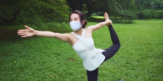 瑜伽教练戴着防护口罩单腿站立，在公园里伸直手