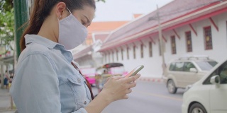 在泰国当地旅行时，使用智能手机应用程序预订和等待她的拼车到达。有吸引力的女性使用手机搜索她的汽车司机在当地地区旅行。独行侠