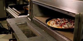 厨师在餐厅厨房里把披萨放进烤箱烤的特写