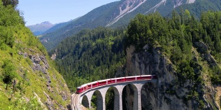 火车在美丽的瑞士山脉中间行驶。列车正驶向一座进入山区的大桥，背景是美丽的风景——4K无人机鸟瞰图