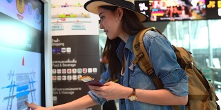 美丽的亚洲女人穿着旅游服装，正在查询航班时刻表。出国旅行可以用于代表独自旅行的概念作品中。