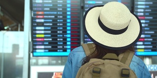穿着旅游服装的美丽亚洲女人浏览航班时刻表的信息板。出国旅行可以用于代表独自旅行的概念作品中。