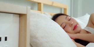 美丽迷人的亚洲女人穿着睡衣闭上眼睛微笑睡觉和甜蜜的梦在卧室的床上在早上感觉如此放松和舒适，保健和睡眠的概念
