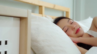 美丽迷人的亚洲女人穿着睡衣闭上眼睛微笑睡觉和甜蜜的梦在卧室的床上在早上感觉如此放松和舒适，保健和睡眠的概念视频素材模板下载