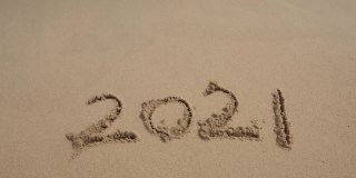 在美丽的海滩背景上的沙子上手写的2021年消息。新年的概念。