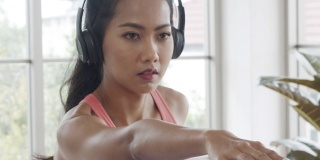 美丽的亚洲女性穿着运动服，戴着耳机听音乐，在家里的客厅里做瑜伽锻炼。