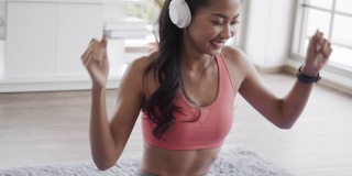 美丽的亚洲女性穿着运动服，一边听音乐一边在家里的客厅里做瑜伽锻炼。