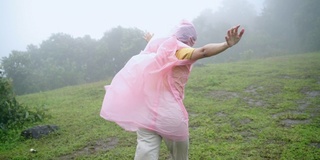 慢镜头后视图的年轻亚洲女子徒步旅行者在雨中与强风吹在山上的小山。美丽的女孩感受自由享受冒险旅行与美丽的自然旅行。