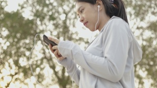 亚洲女性跑步运动员用智能手机听音乐。视频素材模板下载