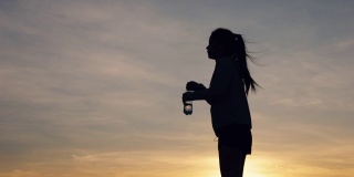 剪影亚洲妇女跑步喝水后，户外日落在山。