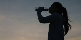 剪影年轻的亚洲女性跑步喝水后，户外日落在山上。