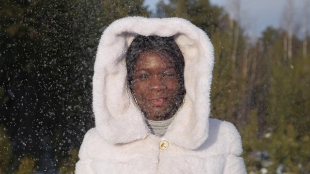 一位非裔美国妇女在闪闪发光的雪下摆姿势微笑