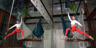 迷人的体贴的年轻女子做空中瑜伽姿势使用吊床。