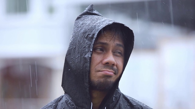 近距离拍摄一个穿着雨衣的年轻人在雨中的慢动作