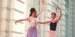 正面图:泰国，阳光明媚的阳光下，一名年轻的女芭蕾舞老师正在教学生，一名正在练习芭蕾舞的白人青少年芭蕾舞者，在当地街道上的一间教室里举起手臂。观念积极的年轻妇女和儿童在周末活动。