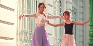 在泰国一个阳光明媚的日子里，年轻的女芭蕾舞老师教学生领导高加索青少年芭蕾舞者跟着练习芭蕾舞举起手臂。概念活泼的年轻妇女和孩子在周末的活动。
