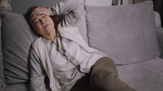 资深亚裔女性坐在家里的沙发上，对自己的生活感到严肃和担忧。老年女性生病或头痛。视频素材模板下载