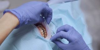 特写的牙医的手在蓝色手套治疗妇女的牙齿戴保护在牙科诊所。保健和医学的概念。
