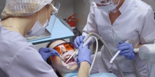 两个年轻的女牙医与眼镜工作的病人刷牙和检查病人，白色外套和面具的特写